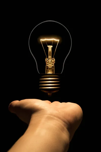 Hand holding a filament lamp on a black background