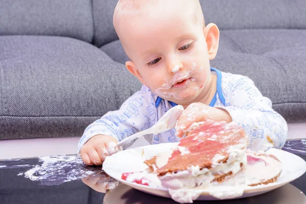First birthday celebration of a little boy. Little boy eating birthday cake with a spoon, happy birthday. Toddler at table with cake. Little baby smash birthday cake.