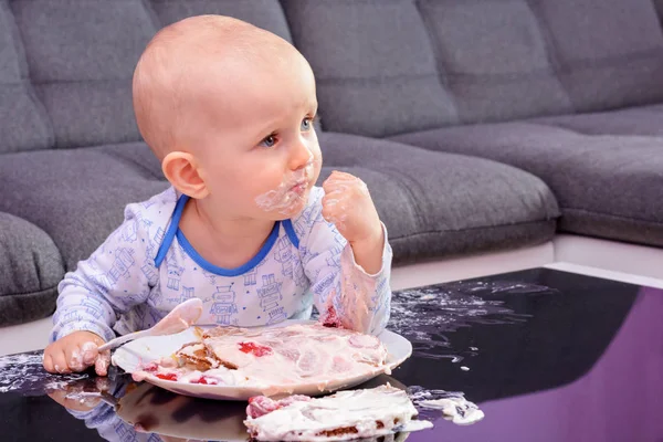 First birthday celebration of a little boy. Little boy eating birthday cake with a spoon, happy birthday. Toddler at table with cake. Little baby smash birthday cake.