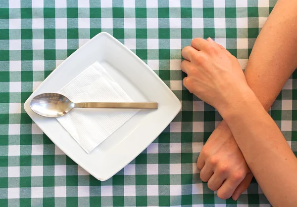 Empty square plate with silver spoon, crossed human hands. — Stock Photo, Image