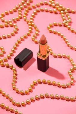 Pembe arkaplanda boncuklarla süslenmiş açık pembe, çıplak mermi ruju..