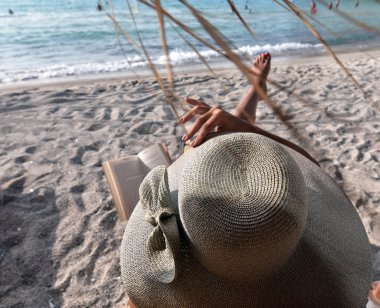 A tourist woman is reading a book and relaxing at the Firopotamos Beach in Milos Island, Greece clipart