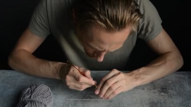 Adam altın kanca ve gri pamuk ipliklerle tığ işi yapmaya başlıyor. Taş masa, ön manzara. Gerçek zamanlı HD stok video görüntüleri.