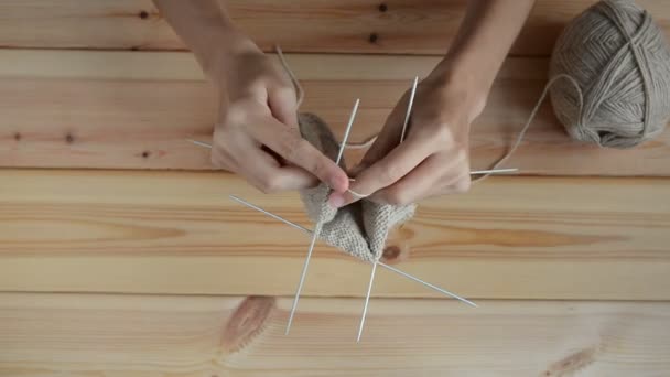 Junge Frauenhände stricken mit grauen Metallnadeln und Wollfäden auf Holztischhintergrund — Stockvideo