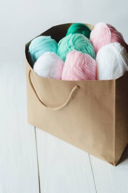 Oval akrilik renkli yün iplik yumakları beyaz tahta arka planda Kraft kağıt kahverengi paketin yanında ve içinde yatar, yukarıdan görünüm, dikey stok fotoğraf