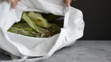 hands of man take and put out ear of corn from fabric tote bag on tabletop
