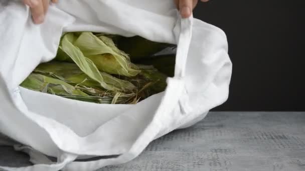 Hands of man take and put out ear of corn from fabric tote bag on tabletop — ストック動画