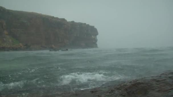 Heavy rain on the surface of the sea against the backdrop of a rocky shore, wide shot. — Stock Video