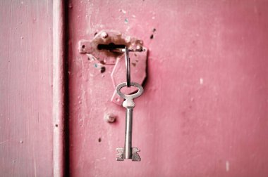Anahtar deliğinde birkaç anahtar var. Pembe metal kapı arkaplanı.