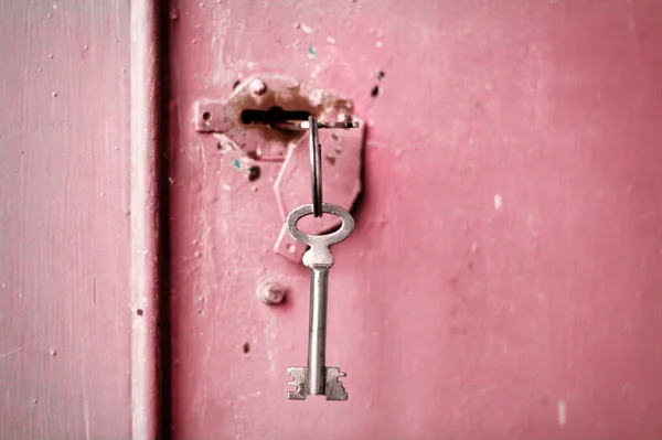 Anahtar deliğinde birkaç anahtar var. Pembe metal kapı arkaplanı.