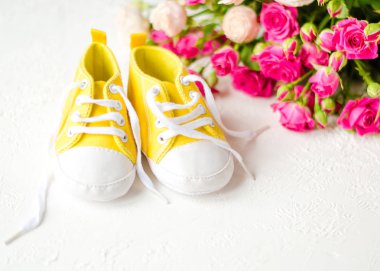 Çocukların sarı ayakkabıları, güllerle beyaz bir masada duruyor. Yakın plan. Çocuk kıyafetleri konsepti. Sarı çizmeli çocukları selamlıyorum. 