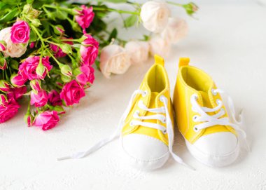 Çocukların sarı ayakkabıları, güllerle beyaz bir masada duruyor. Yakın plan. Çocuk kıyafetleri konsepti. Sarı çizmeli çocukları selamlıyorum. 