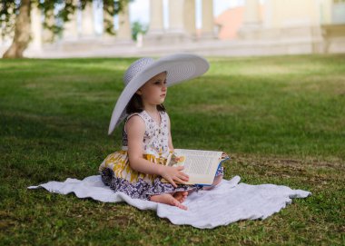 Parkta elinde kitapla hasır şapkalı anaokulu kızı. Parktaki çocuk yaz pikniğinde.