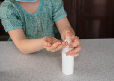 Küçük kız ellerine hijyen spreyi ya da alkol jeli sıkar. Çocuğun elindeki antiseptik temizleme jeli. Kapatın. Koronavirüs salgını sırasında hijyen..