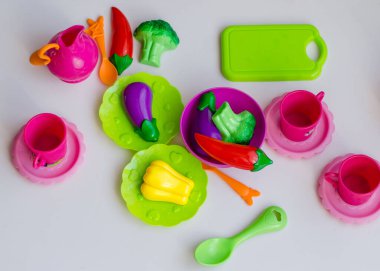 Küçük kız plastik bulaşıklar ve sebze oyuncaklarıyla aşçılık oynuyor. Brokoli, paprika ve patlıcan gibi renkli plastik sebzeli çocukların elleri. Yaklaş, seçici odaklanma