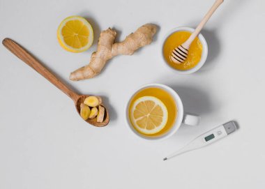 Çay, termometre, zencefil, bal ve limonla bembeyaz arka planda yatıyordu.