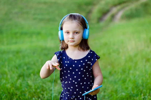 Mała Dziewczynka Niebieskich Słuchawkach Smartfonem Rękach Tańczy Tle Pola Zielonej — Zdjęcie stockowe