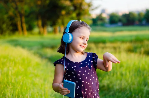 Mała Dziewczynka Niebieskich Słuchawkach Smartfonem Rękach Tańczy Tle Pola Zielonej — Zdjęcie stockowe