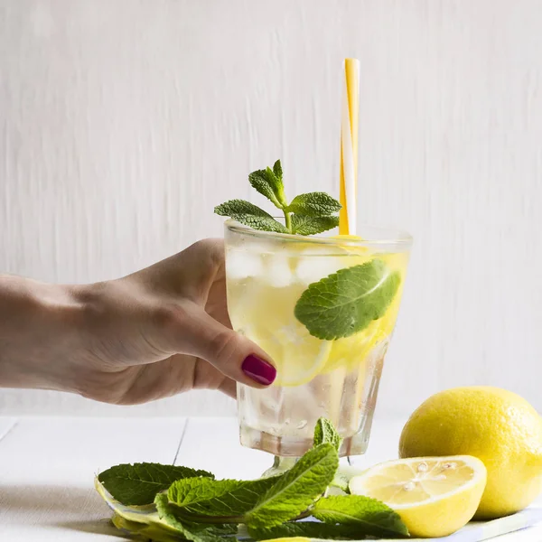 Un vaso de agua desintoxicante con un limón y hojas de menta fresca en la mano de una niña. Estilo de vida saludable . —  Fotos de Stock