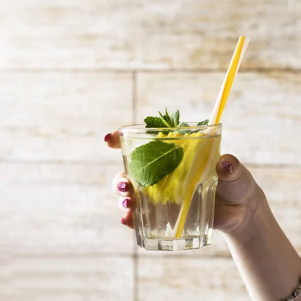 Un vaso de agua desintoxicante con un limón y hojas de menta fresca en la mano de una niña. Estilo de vida saludable . —  Fotos de Stock