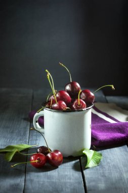 Koyu mavi ahşap arka plan üzerinde bir demir mug içinde Olgun Kiraz.