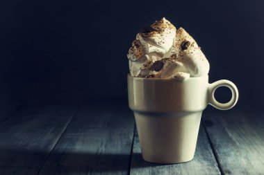 Bir fincan kahve koyu mavi ahşap zemin üzerine krem şanti ile.