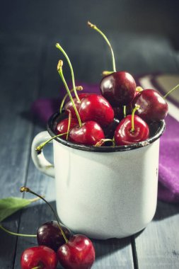 Koyu mavi ahşap arka plan üzerinde bir demir mug içinde Olgun Kiraz.