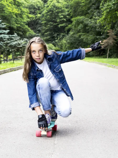 Mooi blonde tiener meisje in jeans overhemd, op skateboard in park — Stockfoto