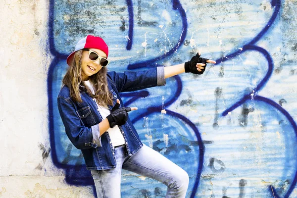 Cute young fair-haired girl teenager in a baseball cap and denim shirt on a stone wall background. — Stock Photo, Image