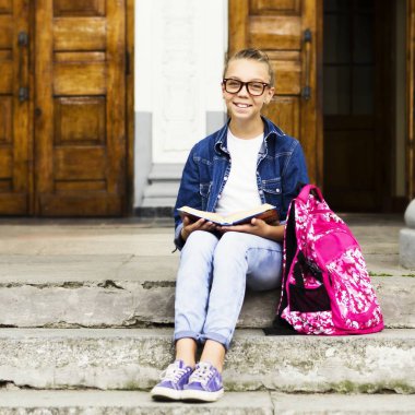 Sevimli sarışın kız kız öğrenci okul yakınındaki otururken bir kitap okuma. Eğitim.