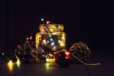 Bir cam kavanoz ve koyu ahşap arka plan üzerinde Noel süsleri parlak çelenk. Yeni yıl, yılbaşı kartpostal. Kopya alanı.