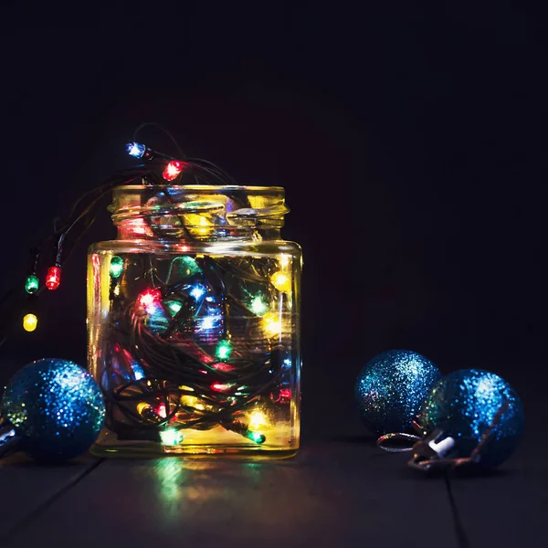 Una ghirlanda incandescente in un barattolo di vetro e decorazioni natalizie su uno sfondo di legno scuro. Capodanno, cartolina di Natale. Copia spazio . — Foto Stock