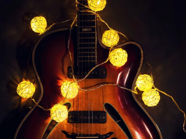 Vieille guitare électrique avec une guirlande éclairée sur un fond sombre. Salutations, Noël, carte de voeux du Nouvel An. Espace de copie . — Photo