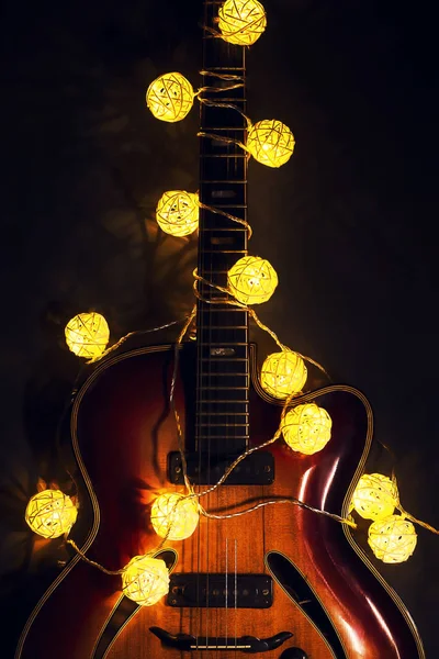 Vieille guitare électrique avec une guirlande éclairée sur un fond sombre. Salutations, Noël, carte de voeux du Nouvel An. Espace de copie . — Photo