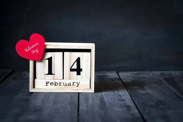 Calendario de madera con la fecha del 14 de febrero, corazón de papel y regalo. Sobre un fondo de madera oscura con espacio para copiar. Día de San Valentín . —  Fotos de Stock