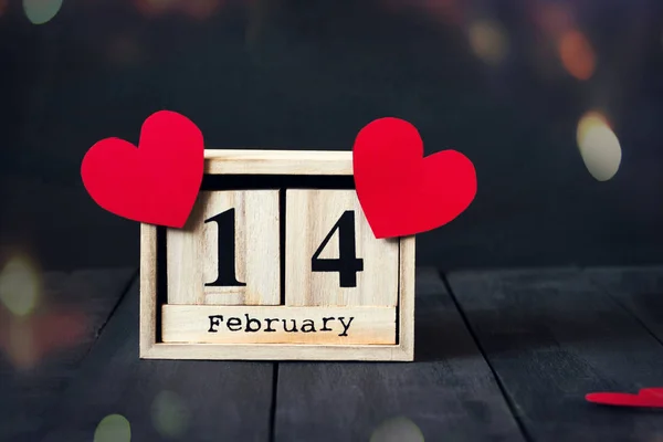 Dřevěný kalendář s datem 14. února, papírové srdce a dárek. Na tmavém pozadí dřevěná s kopie prostoru. Valentinky den. — Stock fotografie