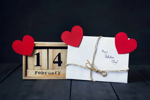 Calendario de madera con la fecha del 14 de febrero, corazón de papel y regalo. Sobre un fondo de madera oscura con espacio para copiar. Día de San Valentín . —  Fotos de Stock