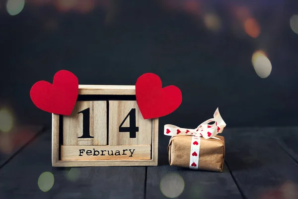 Calendario de madera con la fecha del 14 de febrero, corazón de papel y regalo. Sobre un fondo de madera oscura con espacio para copiar. Día de San Valentín . —  Fotos de Stock