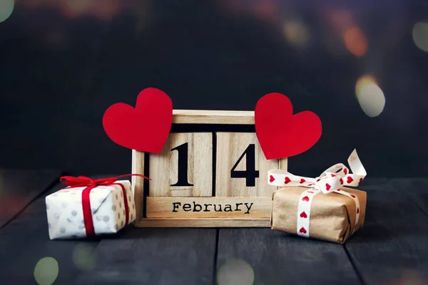 Calendario de madera con la fecha del 14 de febrero, corazón de papel y regalo. Sobre un fondo de madera oscura con espacio para copiar. Día de San Valentín . —  Fotos de Stock