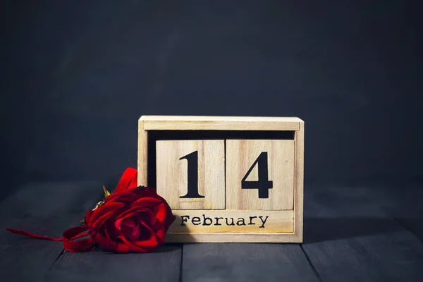 Houten kalender van 14 februari en een rode roos tegen een donkere houten achtergrond met kopie ruimte. Aftelkalender voor Valentijnsdag. — Stockfoto