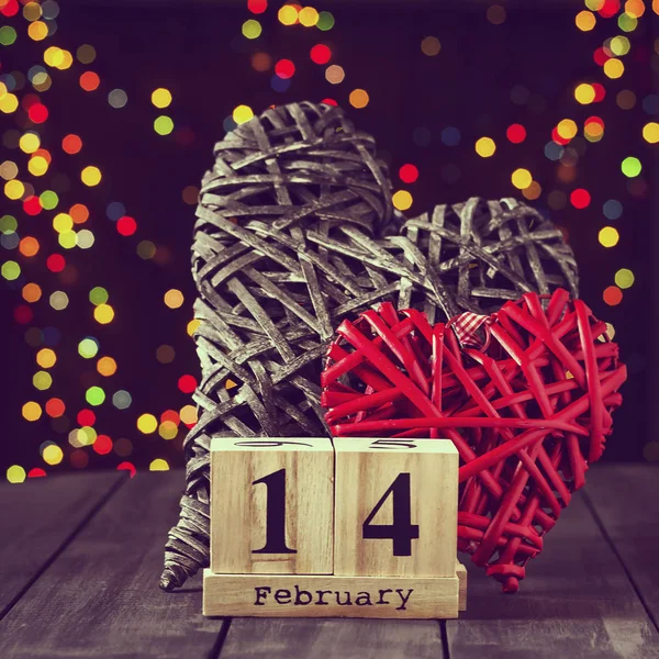 Due cuori di legno e un calendario con una data il 14 febbraio su un tavolo scuro. San Valentino. Copia spazio — Foto Stock