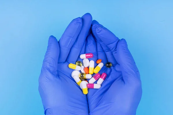 Mavi arka planda elinde tıbbi eldiven olan farklı haplar. İlaçlar. Tedavi. — Stok fotoğraf