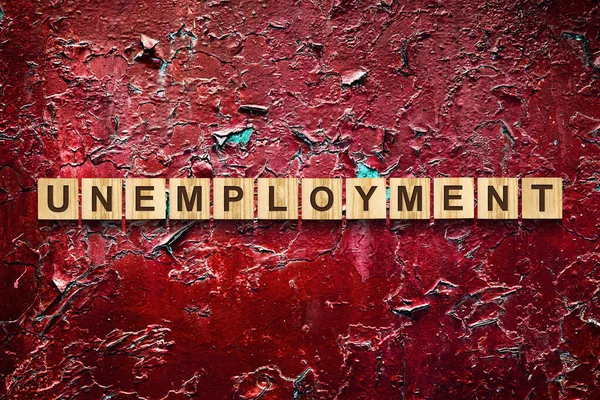 Desemprego. A inscrição em blocos de madeira contra o fundo de uma parede rachada vermelha. Crescimento do desemprego. Negócios . — Fotografia de Stock