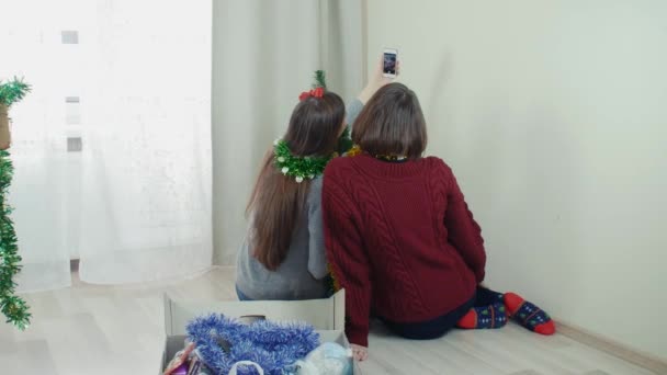 Two young girl preparing Christmas tree for decorations taking selfie having fun — ストック動画