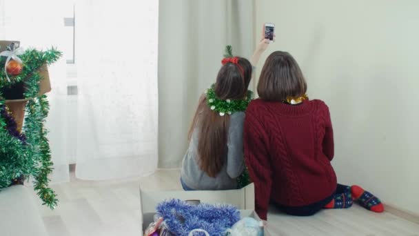 Two young girl preparing Christmas tree for decorations taking selfie having fun — Stockvideo