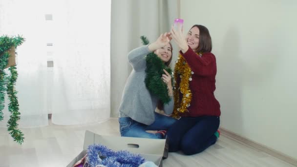 Two young girl preparing Christmas tree for decorations taking selfie having fun — Stock video