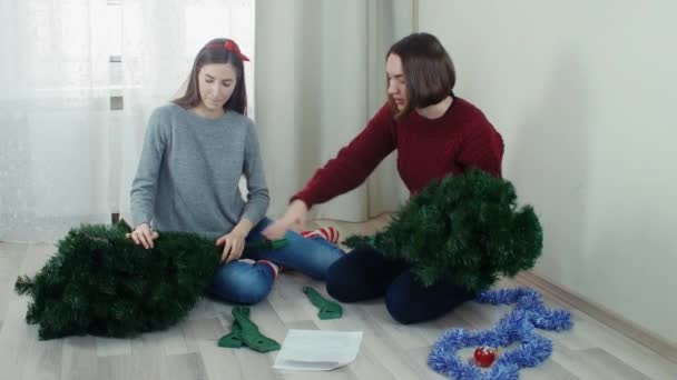 Dos muchacha joven que prepara el árbol de Navidad para adornamientos y que se divierten Nuevo año — Vídeos de Stock