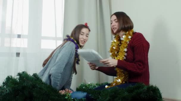 Dos muchacha joven que prepara el árbol de Navidad para adornamientos y que se divierten Nuevo año — Vídeos de Stock