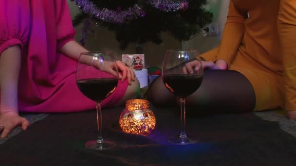 Νεαρό ζευγάρι γυναίκα κάθεται κοντά στο χριστουγεννιάτικο δέντρο με ποτήρια του κρασιού τη διασκέδαση — Αρχείο Βίντεο