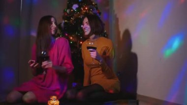 Genç kadın çift bardak şarap ile Noel ağacının yanında oturan